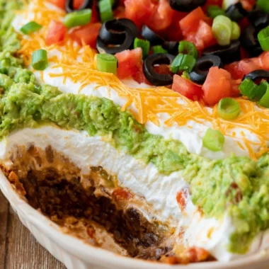Delicious 7 layer dip served in a bowl, featuring layers of beans, guacamole, salsa, and cheese.