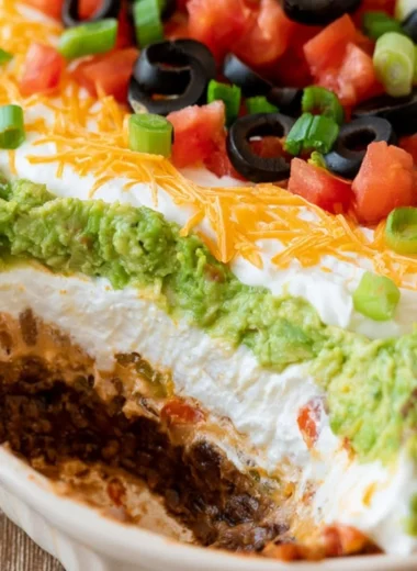Delicious 7 layer dip served in a bowl, featuring layers of beans, guacamole, salsa, and cheese.