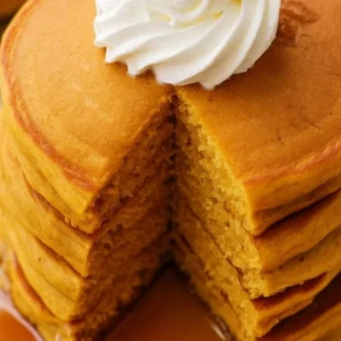 Fluffy pumpkin pancakes stacked on a plate with syrup and spices