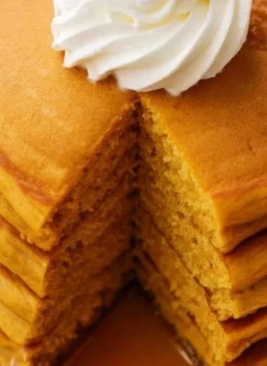 Fluffy pumpkin pancakes stacked on a plate with syrup and spices