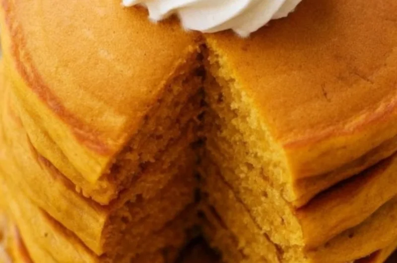 Fluffy pumpkin pancakes stacked on a plate with syrup and spices